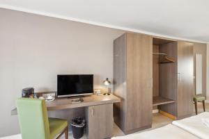 a room with a desk with a television and a bed at Cityhotel Amadeus - 3 Sterne Superior in Münster