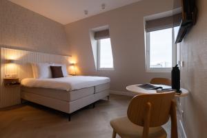 a bedroom with a bed and a desk and two windows at Hotel Zest Den Haag - Scheveningen in Scheveningen