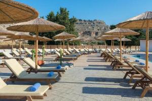 a row of lounge chairs and umbrellas next to a pool at Anavadia Hotel By Anayia All Inclusive Resorts in Kolymbia