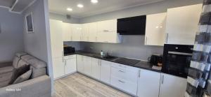 a white kitchen with white cabinets and a couch at Apartament SORENTO 7 in Gorzów Wielkopolski +1 photo