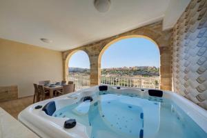 a jacuzzi tub in a room with two windows at Gozo Getaway! Heated Jacuzzi & Views in Xagħra