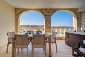 a dining room with a table and chairs and two large windows at Gozo Getaway! Heated Jacuzzi & Views in Xagħra