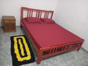 a wooden bed with a red cover and a table at BG Guest House Jaffna in Tirunelveli East