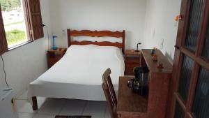 a bedroom with a white bed and a wooden desk at Casa Rosa da Ilha - Suíte com Ar-condicionado e Jardim Amplo in Vera Cruz de Itaparica