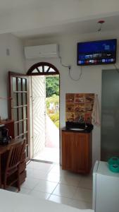 a kitchen with an open door with a television on the wall at Casa Rosa da Ilha - Suíte com Ar-condicionado e Jardim Amplo in Vera Cruz de Itaparica +8 photos