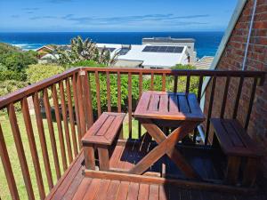a wooden table and bench on a balcony with the ocean at Swallow's Beach in Port Elizabeth