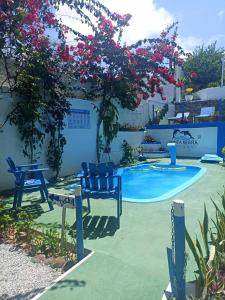 a pool with blue chairs and a tree with pink flowers at Ponta Negra Suites & Apart in Natal