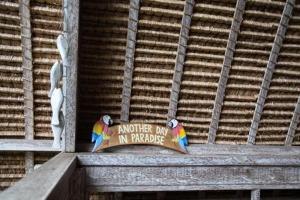 two parrots sitting on a ledge with a sign at Gipsy Beach Bungalows in Sekotong +5 photos