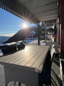 a wooden table and chairs on a deck with the sun shining at Sauna & Mountain Views - Ski-in Ski-out Luxury in Vossevangen