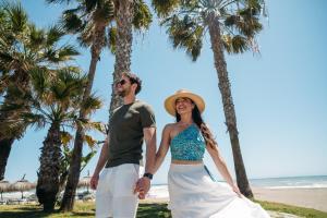 a man and woman standing on the beach with palm trees at Apartamentos MS Puerto Marina, antes MS Pepita in Benalmádena