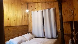 a bedroom with white curtains in a wooden wall at Holo Pousada Vale Encantado in Rancho Queimado