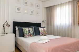 a white bedroom with a bed with pink sheets and pillows at Bellu Suites by GuestPro in Guimarães