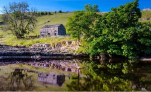 an old barn on a hill next to a body of water at Wharfe Camp Glamping in Kettlewell