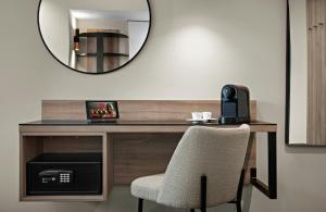 a mirror above a desk with a phone and a chair at Leonardo Hotel Vienna City West in Vienna
