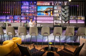 a bar at a restaurant with chairs and a woman at Leonardo Royal Hotel Cologne Bonn Airport in Cologne +86 photos