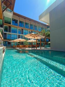 a swimming pool with tables and umbrellas in front of a building at Sunny Hall by AFT in Porto De Galinhas