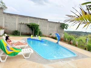 a woman sitting in a chair next to a swimming pool at Chacara Vale do Barreiro in Taubaté