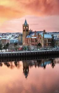 a large building with a clock tower and a river at the foyle bridge apartment in Derry Londonderry
