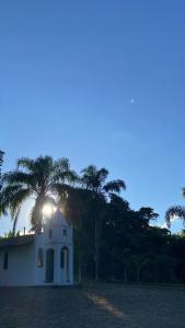 a building with the sun setting behind a group of palm trees at Chalé aconchegante em Resende in Resende