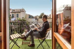a man sitting in a chair reading a newspaper on a balcony at Home Boutique Santa Maria Novella in Florence