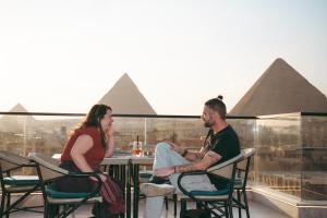 a man and woman sitting at a table with the pyramids in the background at Pharaohs Land Hotel in Cairo