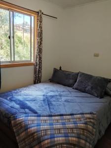 a bedroom with a bed with a blue comforter and a window at Cabañas Doña Magali in Bucalemu
