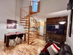 a living room with a dining table and a spiral staircase at La Cachette in LʼAnse-Saint-Jean