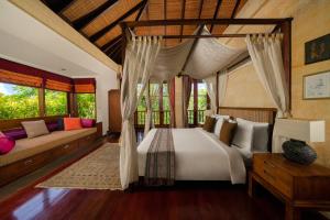 a bedroom with a canopy bed and a couch at Villa Ambiente by Nakula in Jimbaran