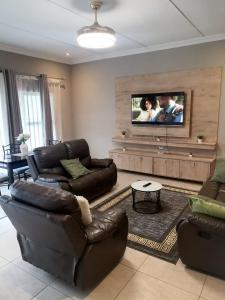 a living room with leather furniture and a flat screen tv at Elegant guest house in Matsapha