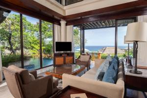 a living room with a couch and a tv and windows at Samabe Bali Villas in Nusa Dua