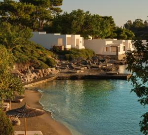 a beach with chairs and umbrellas next to a body of water at Minos Beach Art Hotel, a Member of Design Hotels in Agios Nikolaos