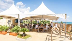 a group of people sitting at tables under a white umbrella at Triscinamare Hotel Residence in Triscina