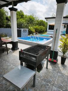 a grill sitting on a patio next to a swimming pool at Anna Homestay Penarik Private Pool in Kampong Ru Sepuloh