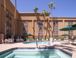 a pool in front of a hotel with tables and umbrellas at GreenTree Inn & Suites Phoenix Sky Harbor in Phoenix