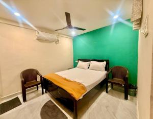 a bedroom with a green wall and a bed and two chairs at Capital Stay Inn in Vijayawāda