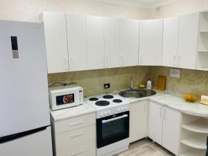 a kitchen with white cabinets and a stove and a microwave at Elegant Home Stepnoy in Karagandy +2 photos