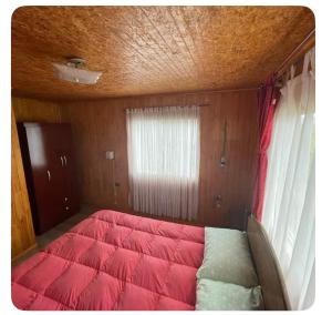 a bed in a room with a red comforter at Cabaña Piola Quilquico in Castro