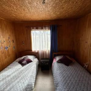 two beds in a small room with a window at Cabaña Piola Quilquico in Castro