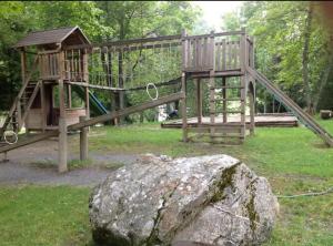 a wooden playground with a rock in the grass at Small bijoux Disentiserhof in Disentis