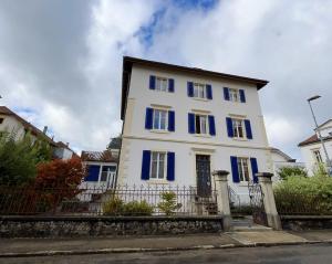 a white house with blue windows and a fence at Appartement Atelier in Le Noirmont