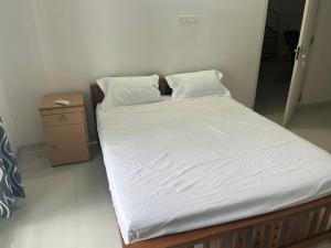 a bed with white sheets and a night stand at THEStay in Alwaye