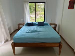 a bed with blue sheets in a room with a window at Casa Marion in Puerto Jiménez