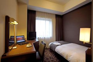 a hotel room with a bed and a desk with a laptop at Hotel Plaza Kachigawa in Kasugai