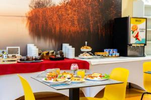 a table with plates of food on it with yellow chairs at Colors Holiday Hotel in Siófok