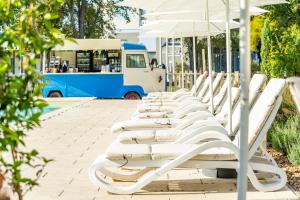 a row of white lounge chairs with an umbrella at Colors Holiday Hotel in Siófok