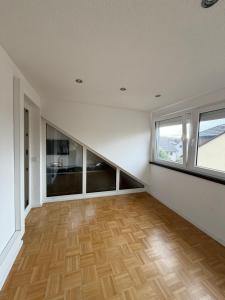 ein leeres Wohnzimmer mit Holzböden und Fenstern in der Unterkunft Modernes Dachgeschossapartment in Singen Zentrum in Singen + 4 Fotos
