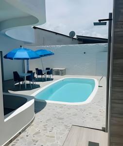 a swimming pool with a table and blue umbrellas at Flats com Temática Grega na Praia de Aruana | Atena Flats in Aracaju