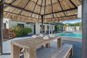 a wooden table with a straw umbrella and a swimming pool at Salinja Cerca 2-B in Palm-Eagle Beach