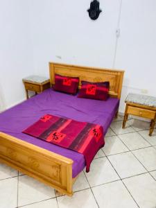 a wooden bed with purple sheets and red pillows at V résidence in Ḩamādat al Kebalou