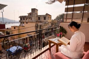 a woman sitting on a balcony reading a book at Sanskriti Vedic Retreat in Rishīkesh